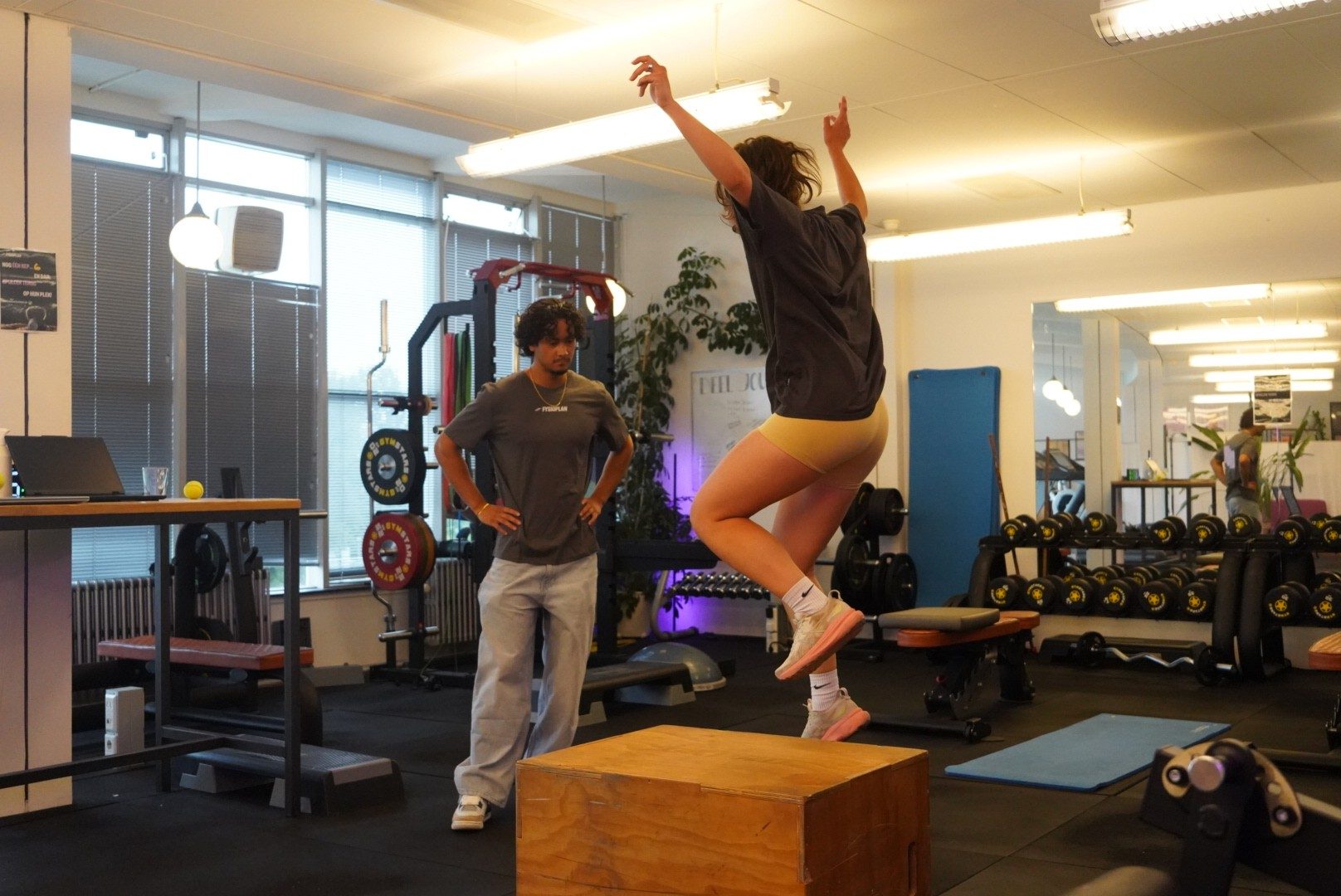 Cliënt doet een sprongoefening in de gym terwijl een fysiotherapeut meekijkt